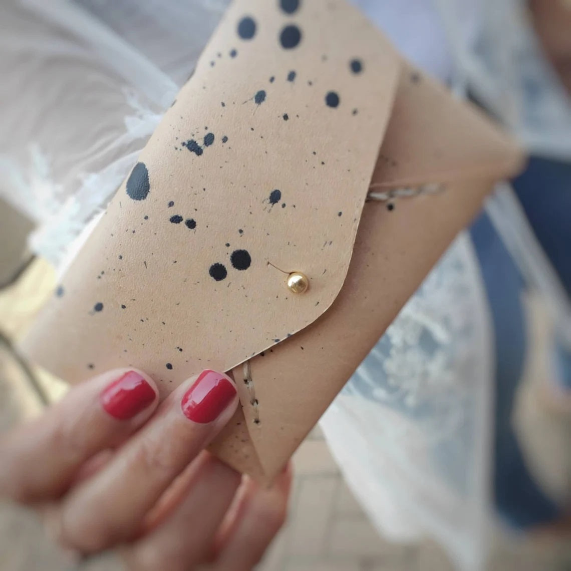 An envelope style card case made out of leather and painted with sweet speckles. Stays closed with a gold metal stud closure
